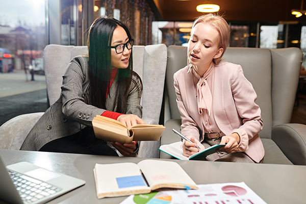 Two young businesswomen have a meeting at cafe, they reading a book and discussing something